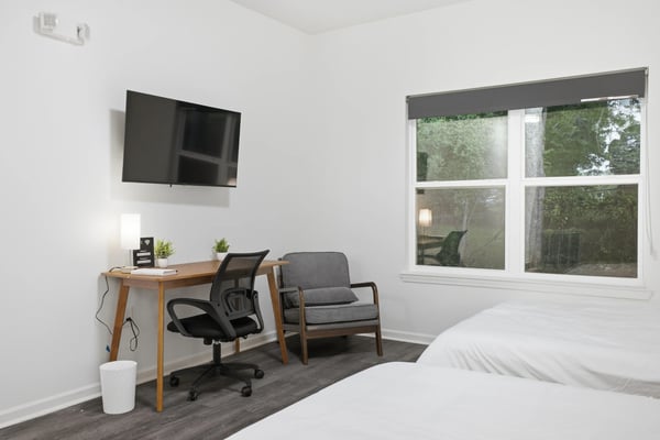 Bright studio bedroom with queen bed, gray armchair, desk, and modern ceiling lights